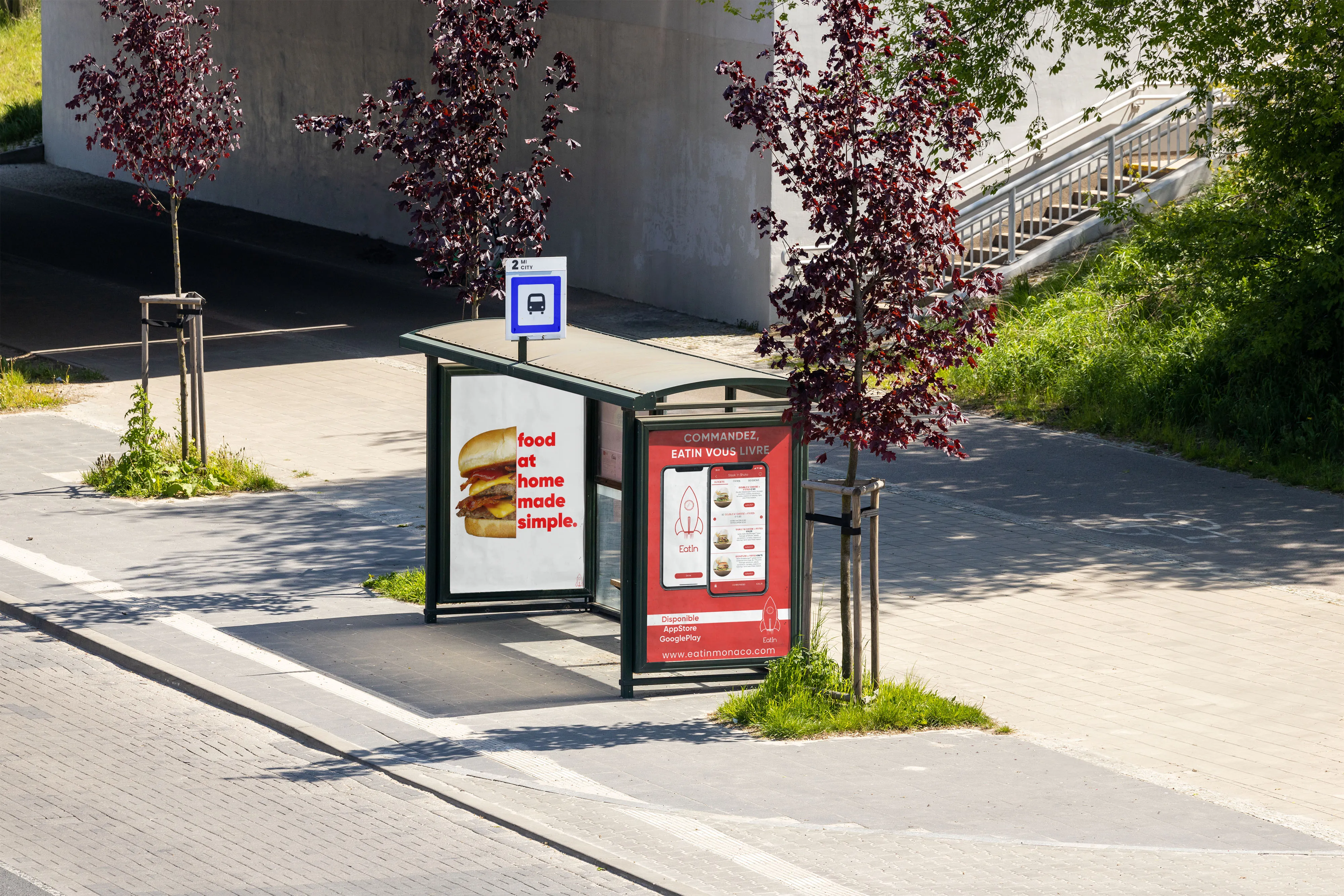 Mockup of a bus shelter on a sunny pavement with two eatin panels: a burger next to the words food at home made simple, and a red panel reading Commandez, eatin vous livre above two phone screens of the app and a rocket logo