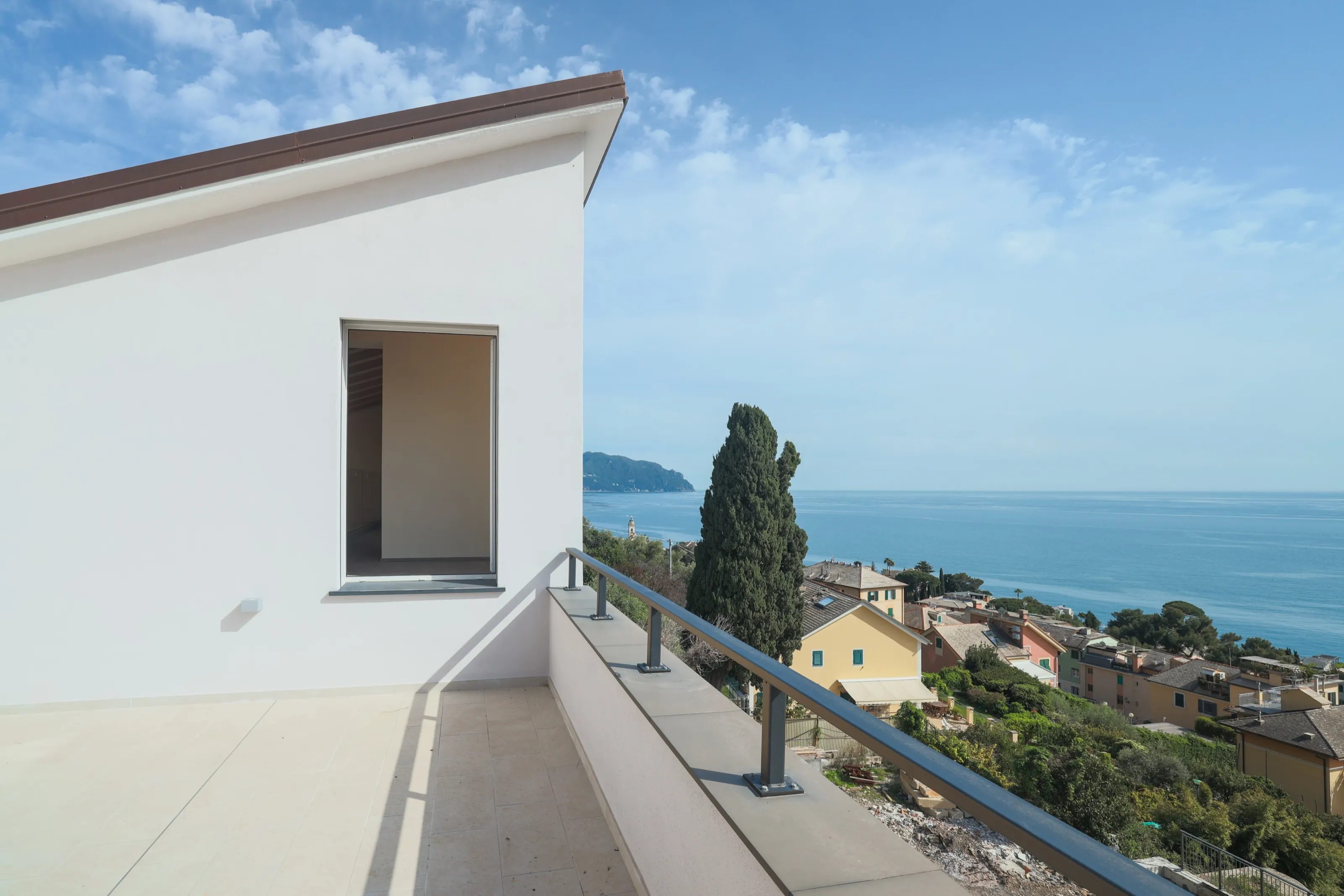 A white terrace of a new house above the Ligurian coast, with a cypress, the village below and the sea