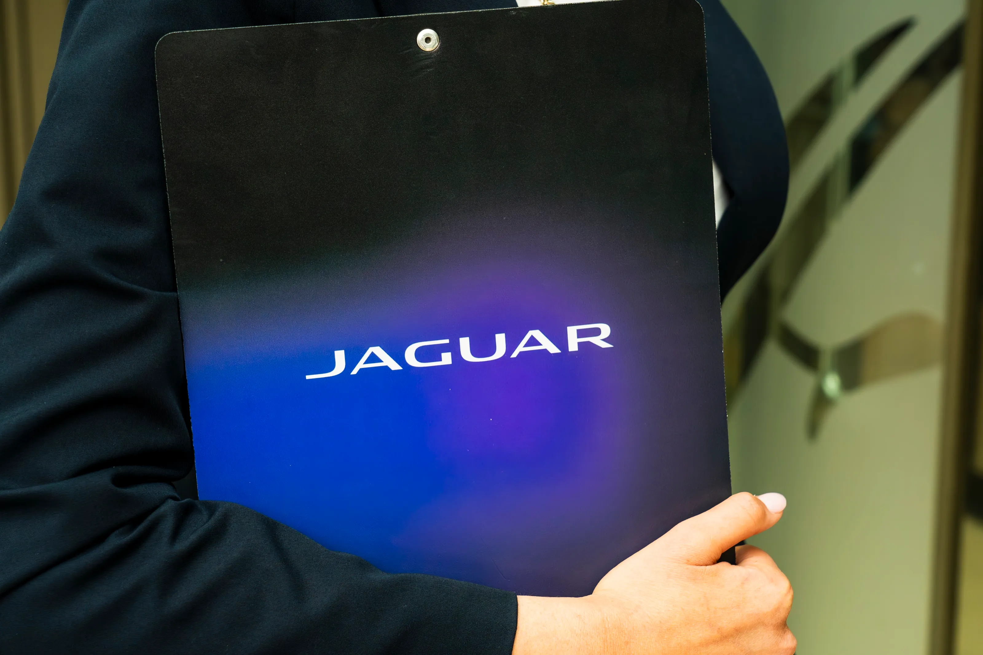 A Jaguar menu card held against a navy jacket, the name in white over a blue and violet glow